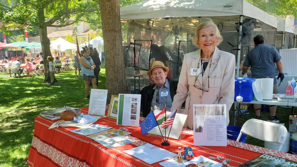 Éva Voisin standing behind the consular information table at the Hungarian Heritage Festival. Sitting next to her is her husband, Paul Voisin.