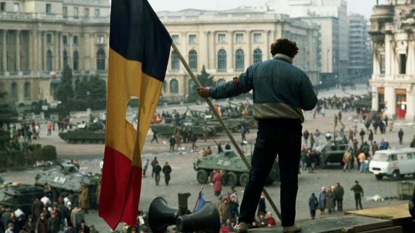 A young man stands on a rooftop in Bucharest during the December Revolution of 1989 with a Romanian flag from which the Communist coat of arms was removed.