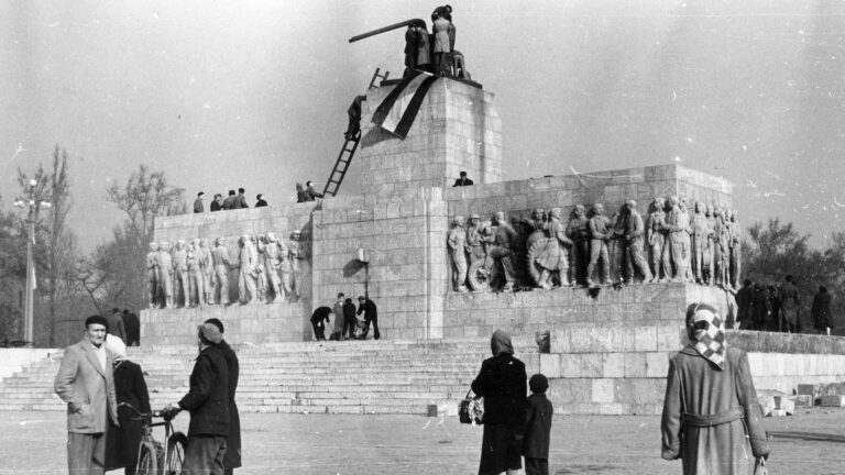 In Budapest, anti-communists and nationalists place a Hungarian national flag atop a demolished statue of Josef Stalin.