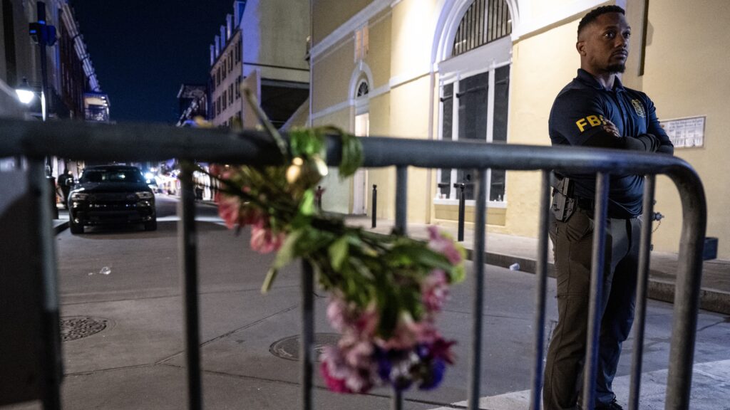 A member of the FBI looks on near a bouquet of flowers tied to a fence, a block from Bourbon Street, after at least 15 people were killed during an attack early in the morning on January 1, 2025 in New Orleans, Louisiana.